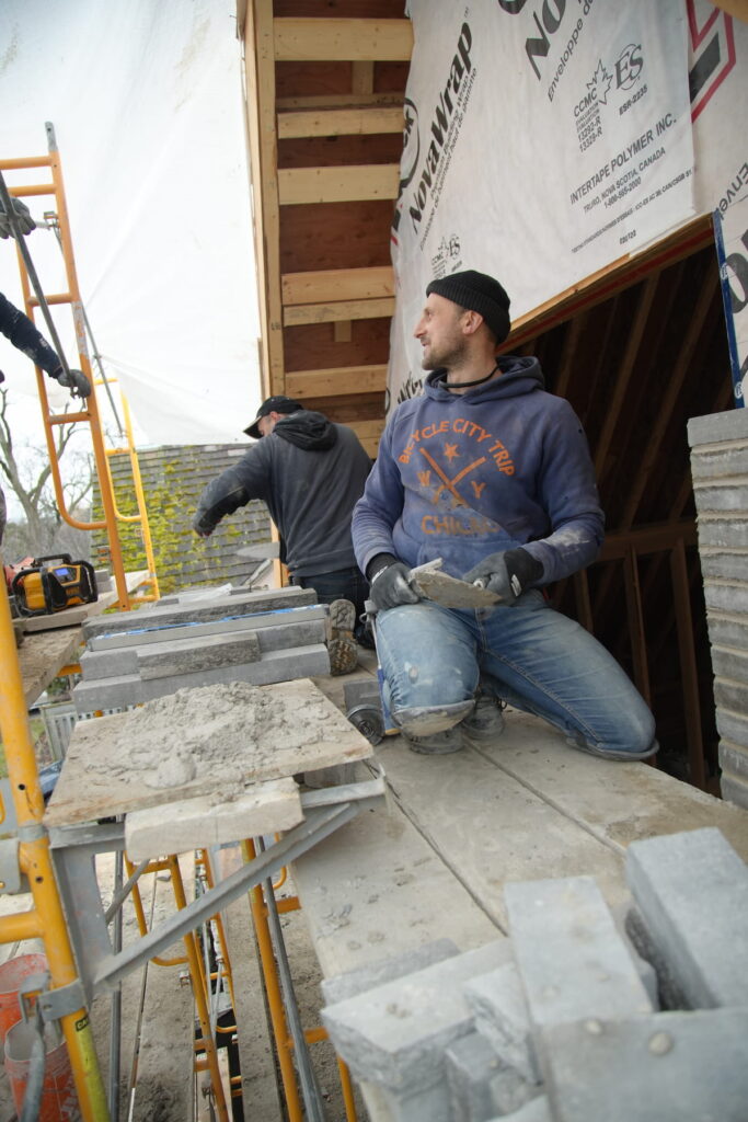 Mason on scaffolding applying mortar beside stone cladding and house wrap on a custom home