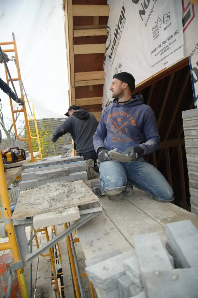 Mason on scaffolding applying mortar beside stone cladding and house wrap on a custom home